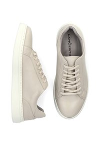 Beżowe skórzane sneakersy z zaokrąglonym noskiem, płaską białą podeszwą i centralnym sznurowanym zapięciem. Gładka textura z minimalnymi detalami przeszycia.