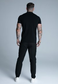 Camiseta negra de manga corta y pantalones cargo negros, con bolsillos laterales, combinados con zapatillas blancas. Textura suave y diseño ajustado.