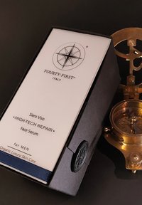 Hoogwaardige gezichtsserumdoos in het zwart met een wit label, met een logo en tekst. Inclusief een ronde messing kompas aan de zijkant.