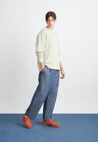 Light green sweater, loose blue trousers, and brown shoes. The clothing features simple design and relaxed fit, with visible stitching details.