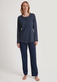 Marineblauwe pyjama set met een lange mouw, gestippeld bovenstuk met knoopsluiting en bijpassende effen broek, gemaakt van zachte stof.