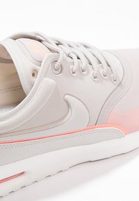 Baskets Nike beige clair en tissu texturé, logo swoosh blanc, lacets blancs, accents roses, et semelle rembourrée vues de profil.