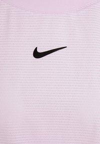 Vaaleanpunainen Nike-urheilupaita, jossa on teksturoitu kuvio ja musta Swoosh-logo keskellä. Paita on valmistettu sileästä kankaasta, ja siinä on pyöreä pääntie.