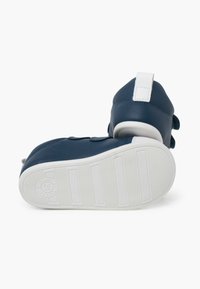 Des chaussures bleu marine avec une tige en cuir lisse, des semelles en caoutchouc blanches, des sangles Velcro et une étiquette en tissu au talon pour un enfilage facile.
