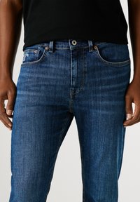 Modré džíny z denimu se střihy rovné nohavice, s klasickým pětipocketovým designem, jemným oděním a kontrastním žlutým prošíváním.