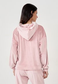 Felpa con cappuccio rosa chiaro realizzata in morbido tessuto peluche, con maniche lunghe e vestibilità comoda. I dettagli includono una tasca a marsupio e cuciture cucite.