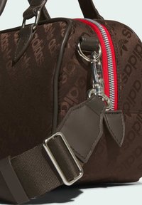 Brown fabric handbag with embossed logo pattern, red zipper, silver hardware, and a detachable brown strap with a metal buckle.