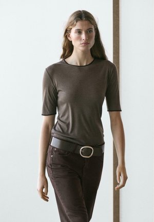 Maglietta aderente marrone con maniche corte, scollo tondo e rifinitura nera. Abbinata a pantaloni marrone scuro e una cintura larga con una grande fibbia circolare.