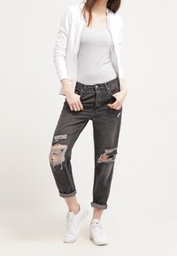 Jeans gris desgastados con acentos rasgados, combinados con una camiseta sin mangas gris clara y una sudadera blanca con cremallera. Calzado: zapatillas blancas.