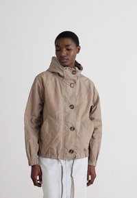 Beige kapucnis dzseki nagy gombokkal, két elülső zsebbel, rugalmas mandzsettákkal és húzózsinóros aljjal. Könnyű anyagból készült.