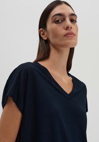 Maglietta blu navy a V con maniche corte, realizzata in tessuto morbido, presenta una vestibilità rilassata e una texture liscia. Design minimalista.