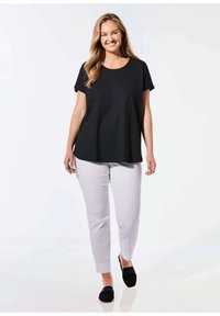 Schwarzes T-Shirt mit kurzen Ärmeln, kombiniert mit hellgrauen, figurbetonten Hosen und schwarzen Slippers. Glattes Material und lockere Passform, mit Rundhalsausschnitt.