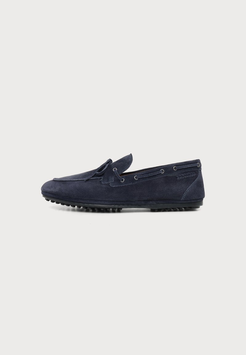 Mocassin de conduite en daim bleu marine avec couture mocassin, détail nœud sur le dessus et semelle en caoutchouc picots pour l’adhérence.