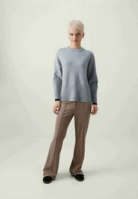 Suéter de mistura de lã azul claro com bainha canelada, usado com calças beges de cintura alta. Textura suave e corte descontraído, combinado com sapatos pretos.