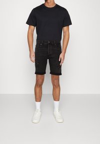 Svart bomull t-shirt i kombination med svarta denimshorts med slitna detaljer vid knäna. Vita sneakers med ljusgrå detaljer och vita strumpor.