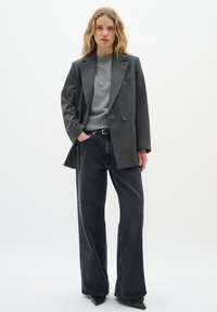 Grå blazer med en enkelt knap, parret med en lysegrå top og højtaljede sorte jeans. Struktureret stof med en struktureret silhuet.