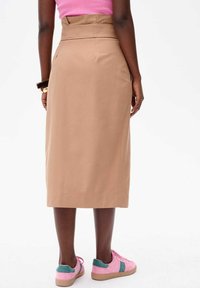 Jupe crayon beige à taille haute et à coupe droite, portée avec des baskets roses présentant des accents en suede vert.