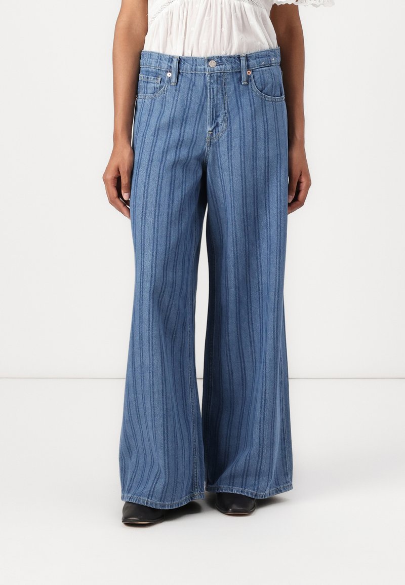 Jeans in denim a gamba larga con righe verticali, di colore azzurro chiaro, e cuciture dettagliate in vita. Presentano tasche e chiusura con bottone.