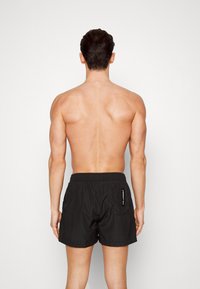 Juodi maudymosi šortai su elastinga juosmens juosta, su šonine kišene ir matomu prekės ženklu gale. Aukštos kokybės, lengvas audinys.