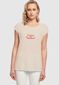 Beige Baumwoll-T-Shirt mit kurzen aufgerollten Ärmeln, das rotes Textdesign mit der Aufschrift "Fröhliche Weihnachten und immer Glücklich" in geschwungener Schrift zeigt.