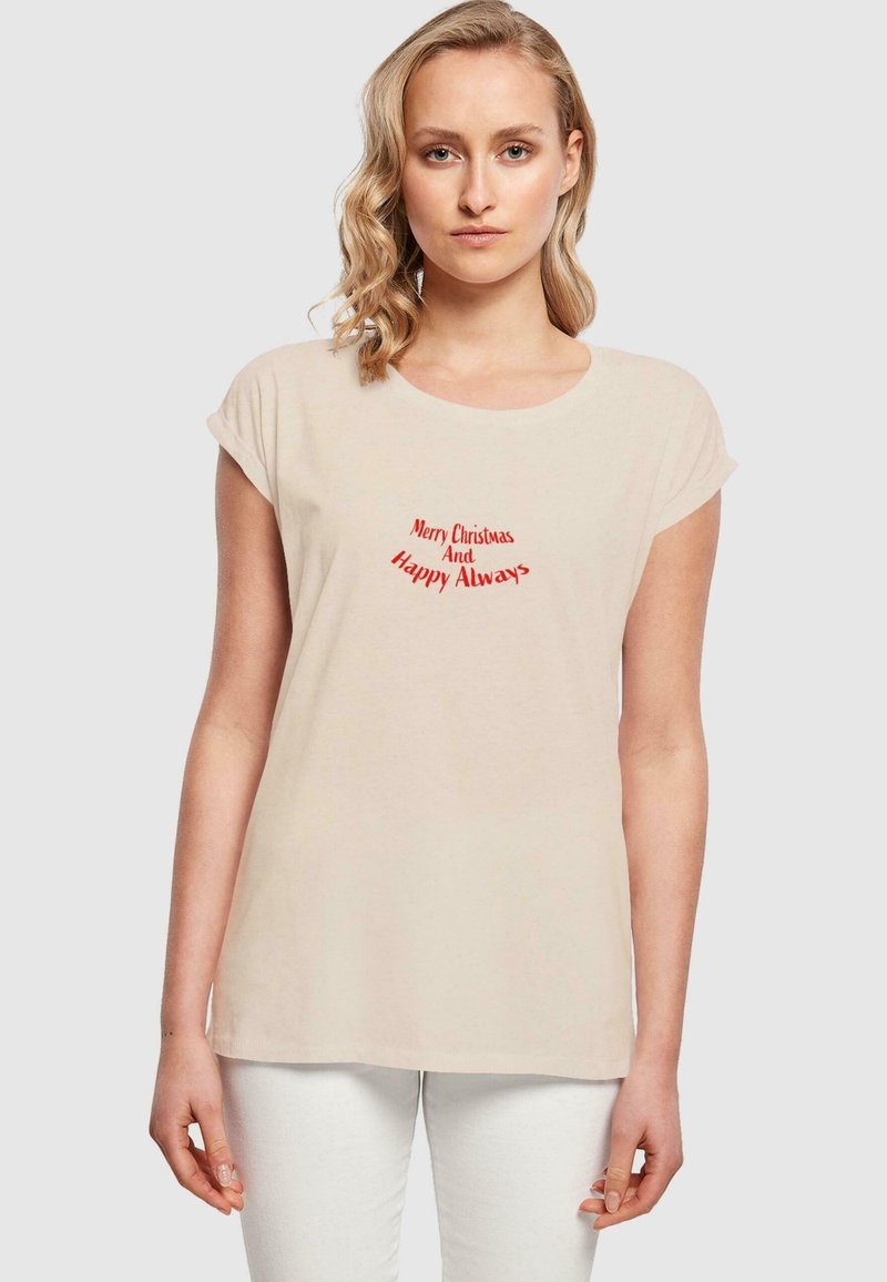 Camiseta de algodón beige con mangas cortas enrolladas, que presenta texto rojo que dice "Feliz Navidad y Siempre Feliz" en un diseño curvado.