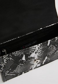 Clutch de diseño en negro y blanco con patrón de piel de serpiente, que presenta un cierre a presión plateado y un interior negro con un bolsillo con cremallera.
