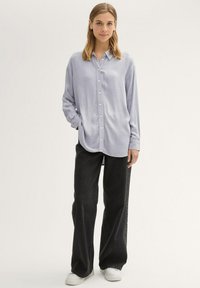 Camicia azzurra chiara con maniche lunghe, abbinata a jeans neri larghi e sneakers bianche. Design semplice, texture morbida, vestibilità casual.