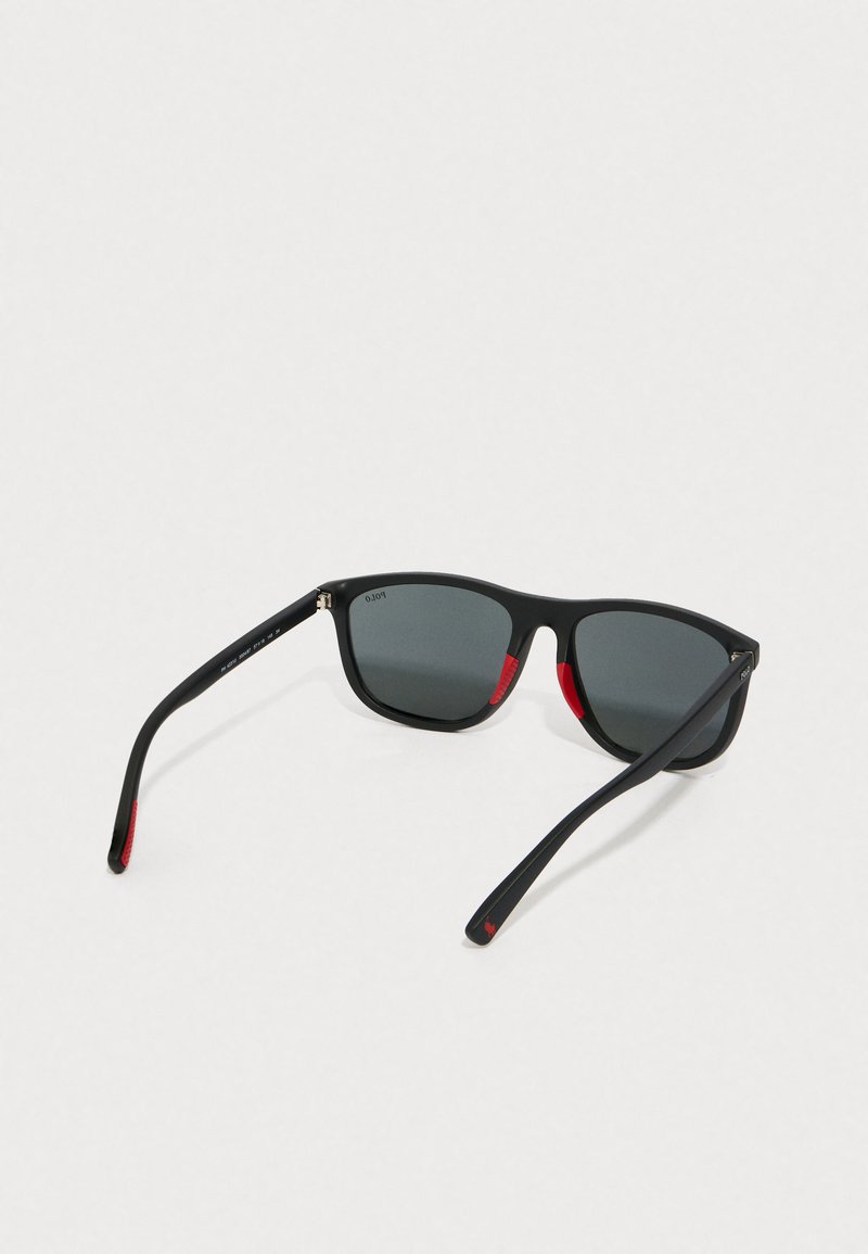 Black plastic sunglasses with grey lenses, featuring red accents on the inner sides of the frames. The design is angular, with straight arms.