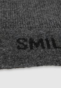 Dunkelgrauer Strickstoff mit einer strukturierten Oberfläche, auf dem das Wort "SMILE" in fetten schwarzen Buchstaben am unteren Rand platziert ist.