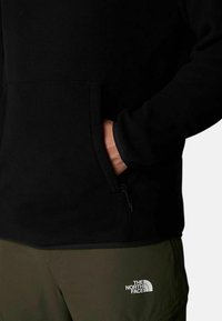 Pullover in pile nero con tasca a marsupio, dotato di dettaglio con zip sul lato e patch con logo in basso a destra.