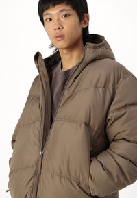 Brown puffer jacket with a hood, featuring a zip front and elastic cuffs. Smooth, slightly glossy material with quilted sections.
