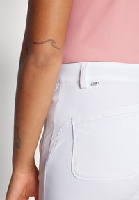 Pantalones blancos con una textura suave y un diseño ajustado, que cuentan con bolsillos traseros y una etiqueta con el logo de CK cerca de la cinturilla.