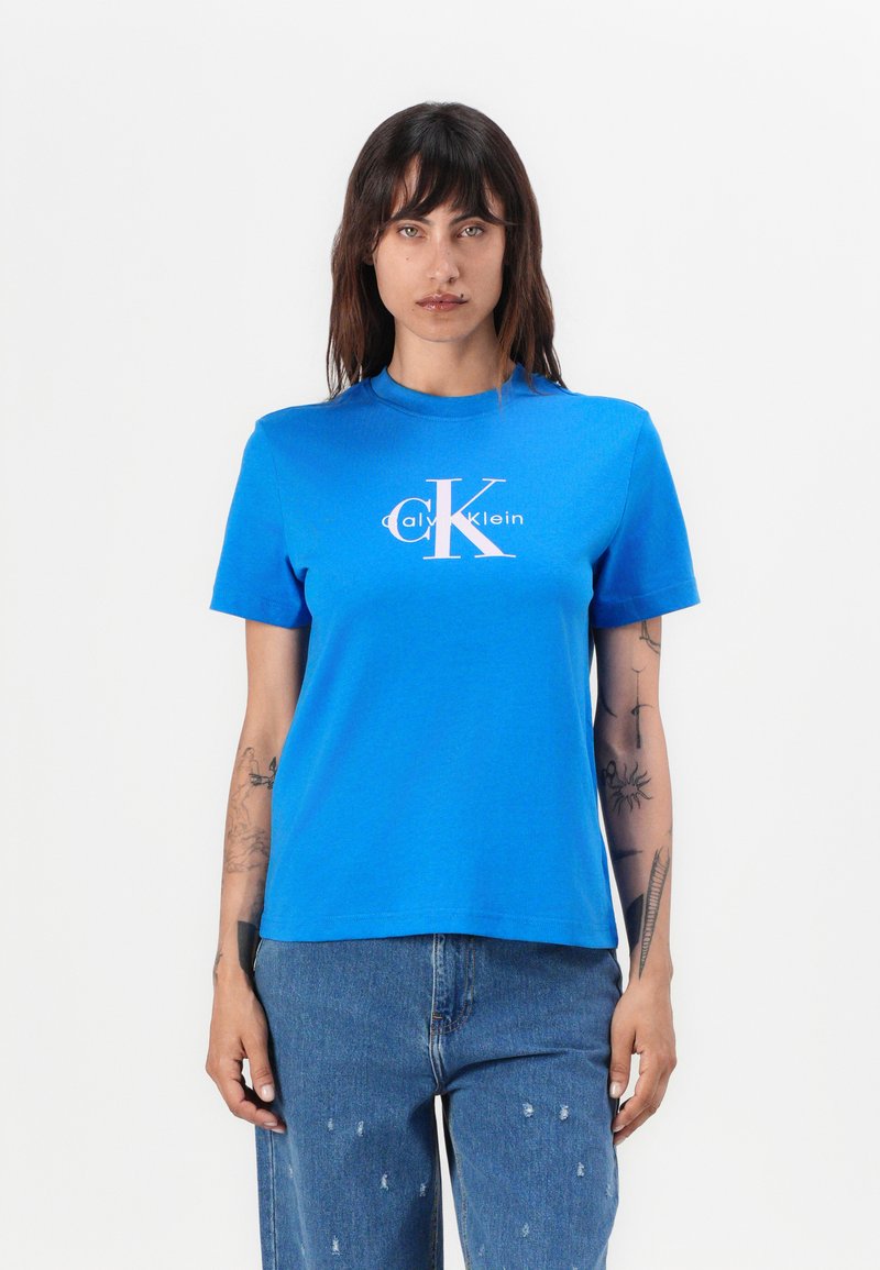 Kortermet blå bomull T-skjorte med en hvit Calvin Klein-logo i midten. Rund hals, avslappet passform, glatt tekstur.