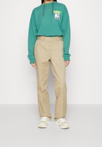 Turquoise langekatoenen shirt met grafische print, beige recht gesneden broek en lichte sneakers met crèmekleurige accenten. Eenvoudige, casual kleding.