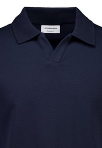 Granatowa koszulka polo wykonana z gładkiej tkaniny, o swobodnym kroju, z płaskim kołnierzykiem i dekoltem w kształcie litery V. Widoczna metka marki "Lindbergh".
