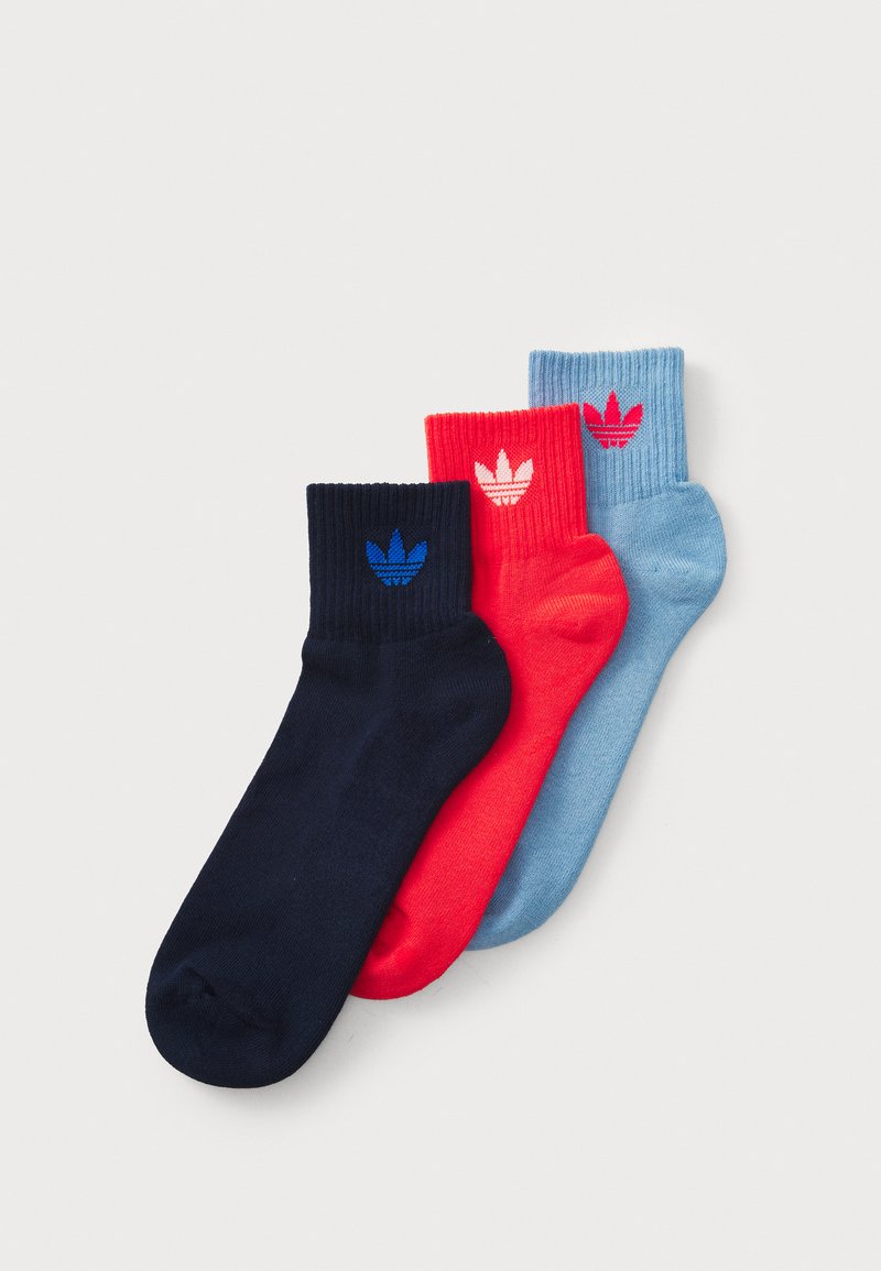 Drie paren enkelsokken in marineblauw, rood en lichtblauw, met ribgebreide boorden en contrasterende logoaccenten op elk paar.