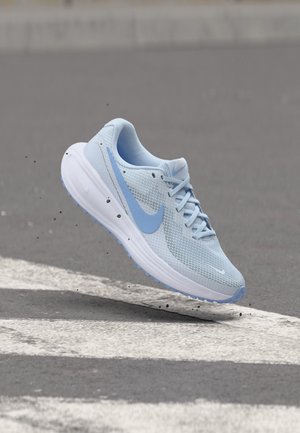 Pantof de alergare Nike albastru deschis cu talpă albă suspendat în aer deasupra unui drum asfaltat cu linii albe de trecere pentru pietoni și diverse resturi mici împrăștiate.