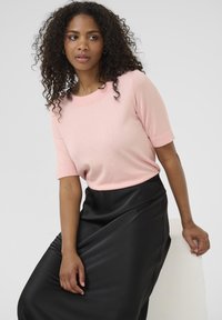 Pull rose à manches courtes en tricot doux, associé à une jupe en simili cuir noir, avec une texture lisse et un léger éclat.