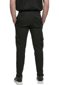 Černé cargo kalhoty vyrobené z bavlny, se bočními kapsami, slim fit a pěti poutky na pásek. Nosené s černobílými teniskami.