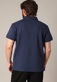 Polo bleu marine à manches courtes, en textile texturé, avec un col et un ourlet côtelés. Présente un design simple et classique sans accents supplémentaires.