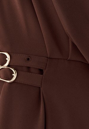 Približni prikaz tamnosmeđe tkanine s dva zlatna ovalna kopča koja pričvršćuju preklapajuće remene.