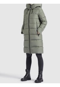 Olive green puffer coat with a hood, full front zipper, and zippered side pockets. Paired with black slim-fit jeans and lace-up ankle boots.