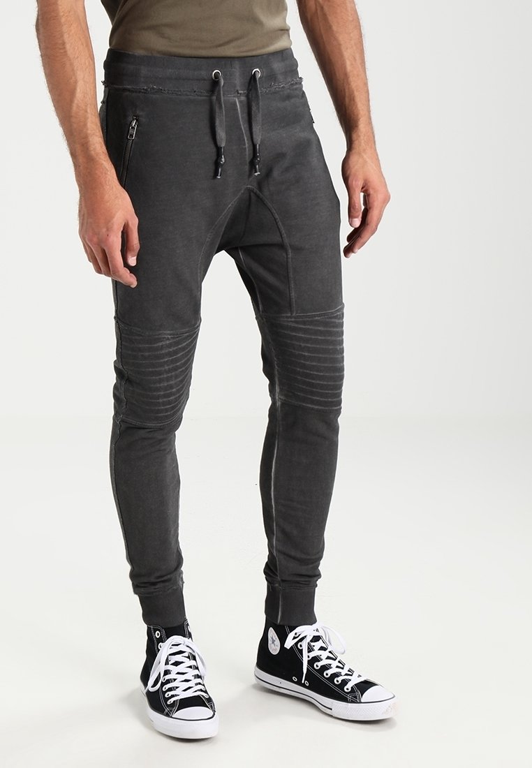 Mörkgrå joggers med dragsko i midjan, ribbad struktur vid knäna och fickor med dragkedja, tillsammans med svarta högstövlar.