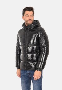 Giacca a vento nera con superficie lucida e trapuntata, cerniera frontale e cappuccio regolabile. Presenta polsini elasticizzati e una tasca sulla manica.