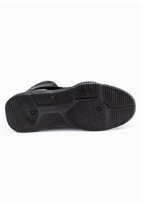 Suola di scarpa nera con materiale in gomma testurizzata, caratterizzata da scanalature per trazione e forma arrotondata. Presenti due indentazioni circolari.