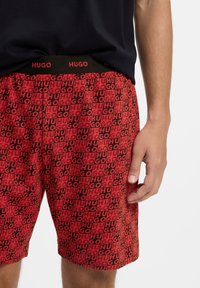 Sarkani šorti ar atkārtotu melnu "HUGO" logotipa rakstu, elastīgs vidukļa jostasvietā. Audums izskatās mīksts un viegls.