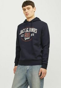 Felpa navy realizzata in un morbido misto cotone, con una stampa del logo in bianco e rosso, tasca a marsupio e cappuccio con cordino.