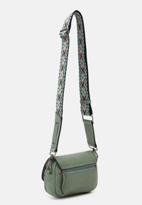 Bolso bandolera de cuero verde con una correa de tela ajustable de color azul verdoso y melocotón con un diseño estampado, y un bolsillo frontal con cremallera.