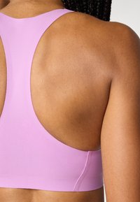 Lys rosa sports-BH med racerback-design, laget av glatt stoff som gir en lett glans, med minimale sømmer og en komfortabel passform.