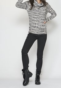 Pull noir et blanc à motifs mouchetés avec col bénitier, associé à un jean noir ajusté et des bottes noires à lacets avec bordure en fourrure et semelles épaisses.